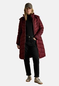 Pikem maroon paksud jackett, mis on varustatud tikandpaneelidega, tõmbluku sulgemise ja kapuužiga. Kantud musta sõrmikuga ja mustade teksadega, koos heledate tossudega.