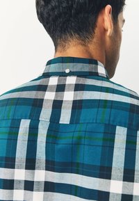 Kariertes Hemd in Blau, Schwarz, Grün und Weiß. Strukturierter Kragen mit Knopfdetail am Ausschnitt.