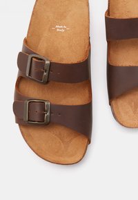 Smeđe kožne sandale s dva podesiva remena i metalnim kopčama. Mekana, teksturirana podstava. Proizvedeno u Italiji.