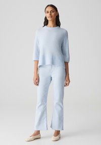 Maglione azzurro chiaro, morbido e lavorato a maglia, con orlo a coste e maniche ampie, abbinato a jeans azzurri chiari a gamba dritta e scarpe beige senza lacci.