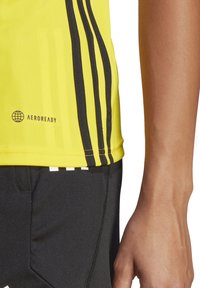 Geel sportshirt met zwarte strepen, AEROREADY merkuiting en een zachte textuur, gecombineerd met zwarte shorts met subtiele zakdetails.