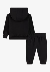 Tuta in cotone nero con felpa con cappuccio dotata di polsini e fascia in vita a coste, abbinata a pantaloni affusolati coordinati. Texture liscia su tutta la superficie.