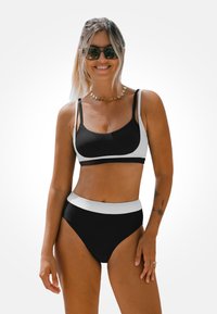 Schwarzes und weißes Bikini-Set mit einem strukturierten Bralette-Oberteil mit verstellbaren Trägern und hoch geschnittenen Unterteilen mit einem kontrastierenden Bund.