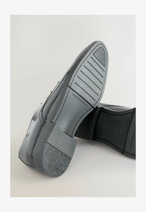 Schwarze Lacklederschuhe mit glatter Oberfläche, niedrigem Absatz, Gummisohle, elastischen seitlichen Akzenten und strukturiertem grauen Fersenaufsatz.