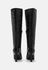 Bottes noires en cuir jusqu'au genou avec une texture lisse, des talons carrés et des zips sur le côté. Présentent un design ajusté qui accentue la forme des jambes.