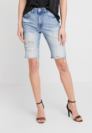 Vrouw draagt lichtblauwe versleten denim Bermuda-shorts gecombineerd met een zwarte top en hooggehakte sandalen met luipaardprint.