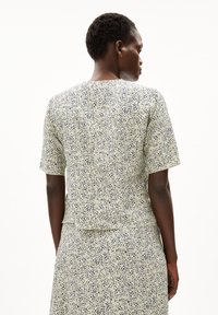 Kurzarmbluse in Hellgrün mit dunkelblauen abstrakten Mustern, featuring einem runden Ausschnitt und einem lockeren Schnitt, hergestellt aus einem glatten Stoff.