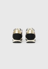 Black sneakers with a sleek design, featuring a white sole, gold accents, and a textured fabric toe. Back view highlights brand logo.