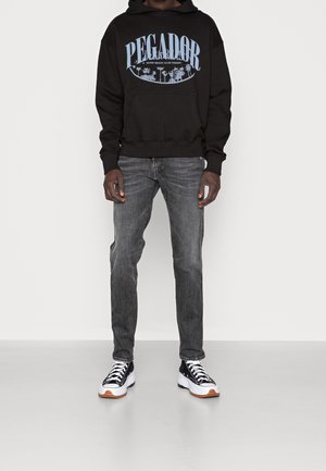 Sudadera negra con el logo azul "PEGA DOR", jeans grises y zapatillas en blanco y negro con suelas naranjas. Diseño simple, ajuste casual, material de algodón.