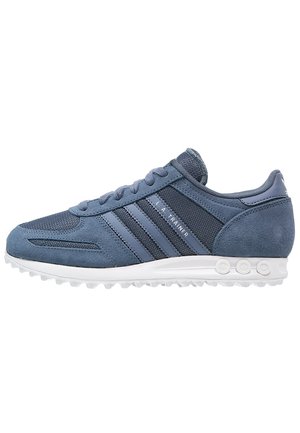Baskets de sport en daim bleu et mesh avec semelle blanche, trois bandes sur le côté et texte "L.A. Trainer" près des lacets.