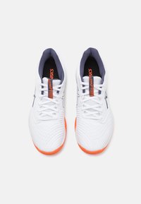 Zapatos deportivos blancos con una parte superior texturizada, acentos naranjas en la suela y un interior azul marino. Presentan cordones redondos y un detalle de logo.
