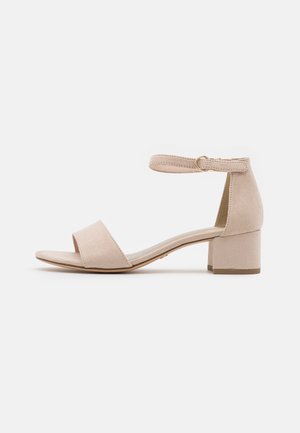 Beige suede sandal with an open toe, wide strap over the foot, and a buckled ankle strap, featuring a short, square block heel.