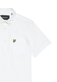 Camicia bianca a maniche corte in cotone con colletto a punta, caratterizzata da una farfalla gialla ricamata sulla tasca del petto.