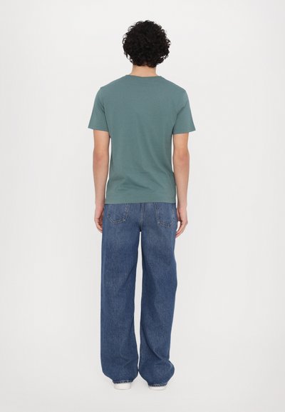 T-shirt en coton vert avec un col rond, des manches courtes et une coupe décontractée, associé à un jean bleu foncé à coupe ample.