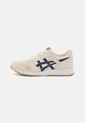 Chaussure de sport beige avec accents noirs, matériaux en mesh et daim, bout arrondi et semelle en caoutchouc. Présente un marquage distinctif sur la languette.