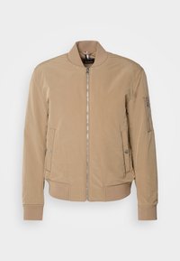 Beige bomberjacka med dragkedja fram, ribbade ärmslut och två sidofickor, med en mjuk textur och minimalistisk design.