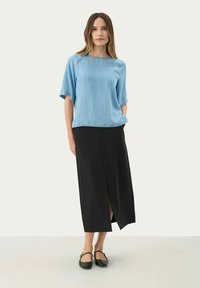 Blå kortærmet bluse kombineret med en sort maxi-nederdel med en forslidse. Blusen har en blød tekstur; outfittet er minimalistisk og moderne.