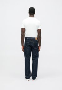 Σκούρα μπλε τζιν με ίσια γραμμή, διακοσμημένα με δερμάτινο ταμπελάκι στη μέση και διακριτικές ραφές. Συνδυάζονται με απλό λευκό τζην.