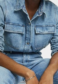 Ljusblå denimskjorta med knapplist framtill, krage och två bröstfickor. Tyget har en klassisk texturerad finish.