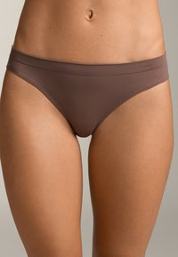 Rjav bikini spodnjice z gladko teksturo, nizkim rezom in širokim elastičnim pasom. Ponaša se s minimalnim logotipom vtisnjenim na strani.