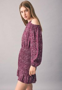 Fialová off-shoulder šaty s kvetinovými vzormi, vyhrnutými rukávmi a gumičkovým pásom s volánovým lemom. Mäkká, ľahká tkanina.