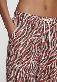 Losse broek met een golvend patroon in rood, zwart, wit en beige. Gemaakt van zachte stof met een elastische tailleband en zijzakken.