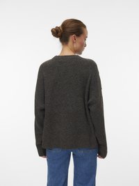 Maglione lavorato a maglia di colore marrone scuro con una vestibilità comoda, orlo a coste e maniche lunghe. Indossato con jeans in denim blu, visto da dietro.