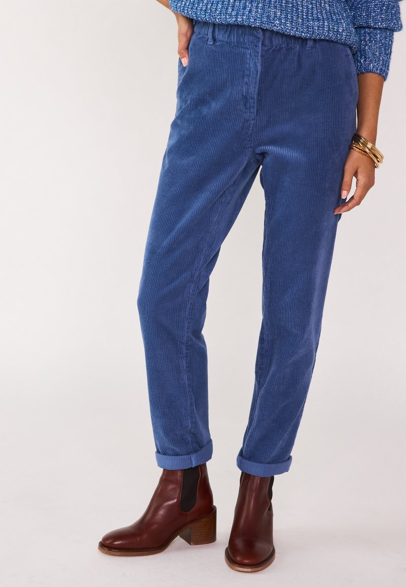 Pantaloni in corduroy blu con vestibilità ampia e orli arrotolati, dotati di tasche laterali. Abbinati a stivaletti in pelle marrone.