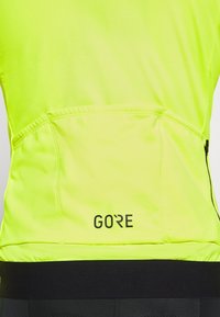 Top atletico giallo brillante con un design aderente. Presenta un elastico nero in vita e un logo sul retro. Tessuto morbido e tasca con zip.