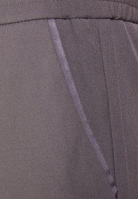 Gros plan sur un tissu gris à la texture lisse, présentant une couture latérale et un fin accent rayé.