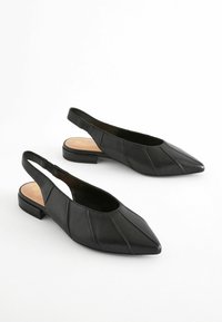 Fekete bőr feltartó cipők hegyes orral, varrott panel részletekkel és alacsony blokksarkakkal. Simább felület minimális díszítésekkel.