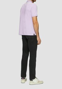 Lilafarbene Poloshirt mit kurzen Ärmeln, kombiniert mit schwarzen Jeans und weißen Sneakers. Das Shirt hat einen klassischen Kragen und seitliche Schlitze.