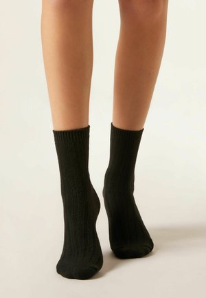 Svarta ribbade ankelsockor med en mjuk textur, med vikta manschetter och en snug passform runt fötterna. Lämpliga för avslappnad användning.