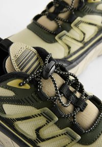 Sneakers sznurowane z beżową i oliwkową siateczką, czarnymi akcentami oraz gumową podeszwą z teksturowanym wzorem.