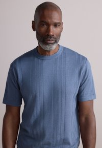 Pull en maille ajusté à manches courtes, de couleur bleu clair. Présente une texture côtelée verticale et un col arrondi, confectionné dans un tissu doux et respirant.