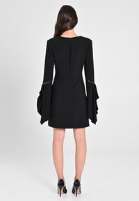 Schwarzes Kleid mit langen, glockenförmigen Ärmeln und einer taillierten Silhouette. Verfügt über einen Reißverschluss auf der Rückseite und dezente metallische Akzente an den Ärmelöffnungen.