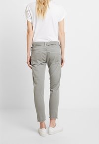 Ljusgrå tapered-byxor med rå nederkant, bakfickor och mjukt tyg. Matchas med en enkel vit t-shirt och vita slip-on skor.