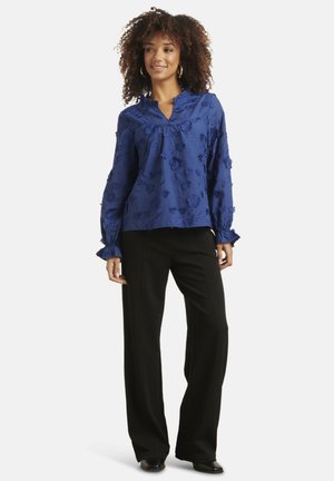 Blue floral embroidered blouse with ruffled collar and long sleeves, paired with black wide-leg trousers and black shoes.