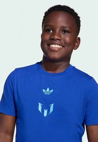 T-shirt azul de algodão com logótipo Adidas azul claro e design gráfico no peito, gola redonda e mangas curtas.