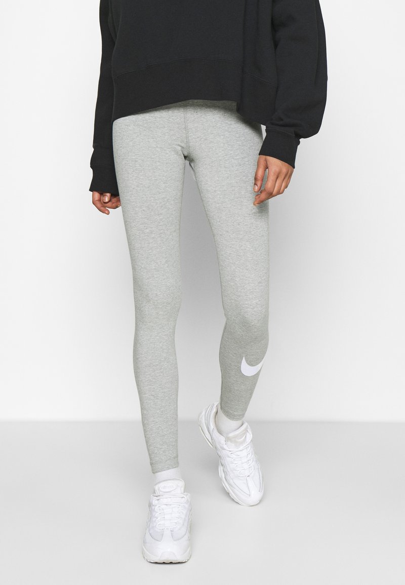 Leggings atletici grigio chiaro realizzati in tessuto elasticizzato, con un logo Nike bianco sul polpaccio sinistro. Indossati con una felpa nera oversize.