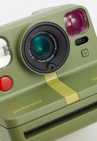 Green plastic Polaroid camera with a round lens, red button, and yellow accent. Features autofocus and a filter sensor. Compact, modern design.