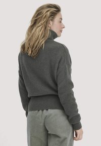 Dunkelgrauer gestrickter Pullover mit hohem Kragen und geripptem Saum, der eine lockere Passform und eine strukturierte Oberfläche bietet, kombiniert mit hellgrünen Cordhosen.