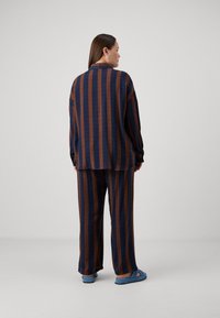 Dryžuota laisvalaikio apranga, kurią sudaro tamsiai mėlynos ir rudos spalvų, laisvai krentanti marškinėliai su ilgomis rankovėmis ir derančios plačios kelnės.