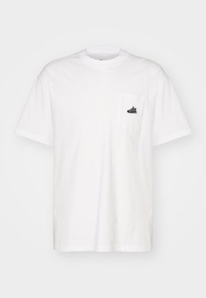Camiseta de algodón blanca, con cuello redondo, mangas cortas, presenta un bolsillo en el pecho izquierdo con un pequeño detalle del logo en negro. Diseño simple y sin adornos.