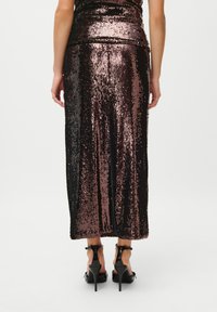 Sidabrinė sijonas su vertikaliomis juostelėmis juodos ir rožinės spalvos, iki kelių ilgio, su prigludusia siluetu, derinamas su juodais aukštakulniais.