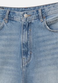 Lichtblauwe spijkerbroek in close-up, met zicht op de voorste knoop, riemlussen, bovenkant van de rits en voorzakken met zichtbare stiksel-details.