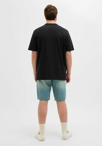 Camiseta de algodón negra de manga corta, combinada con pantalones cortos de denim azul claro. El modelo lleva zapatillas blancas y calcetas crema.