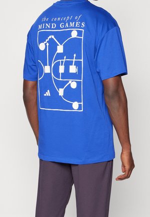 Mann trägt ein blaues T-Shirt mit Basketballfeld-Spiel-Diagramm und dem Text „das Konzept von MIND GAMES“ auf dem Rücken.