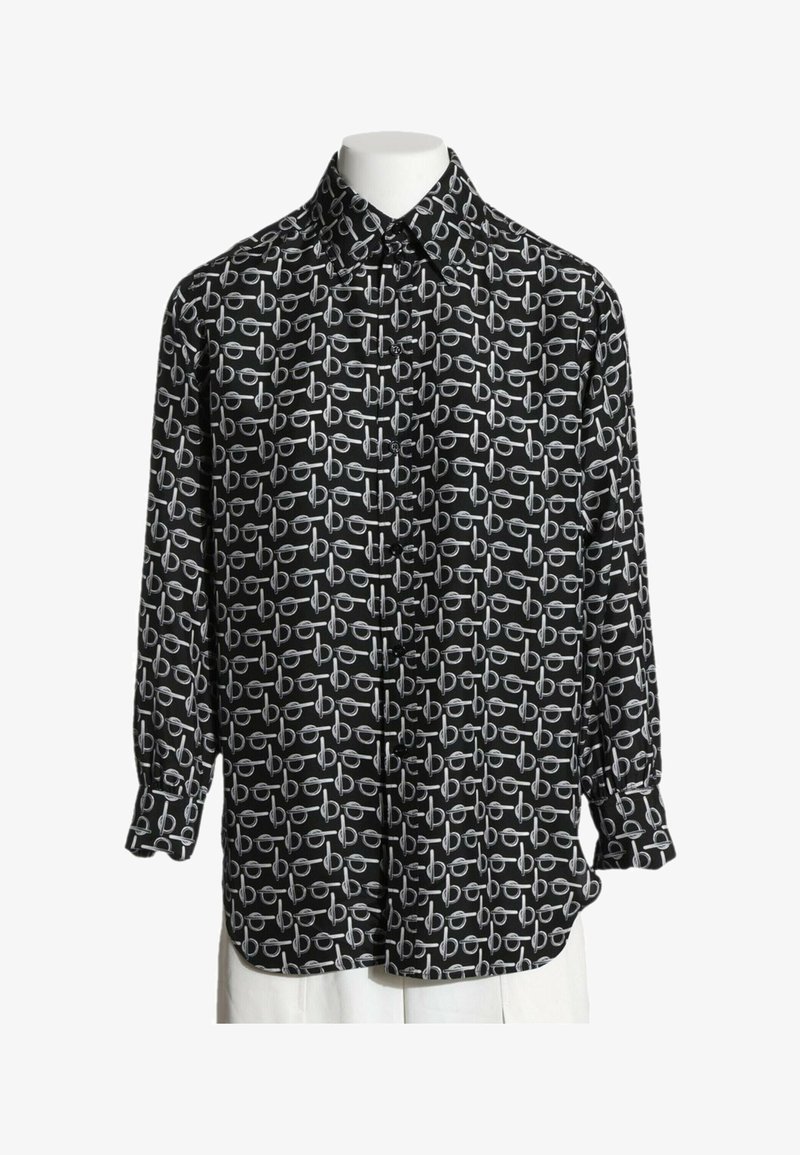 Chemise noire à manches longues boutonnée avec un motif abstrait circulaire et des lignes horizontales blanches sur un torse de mannequin blanc.