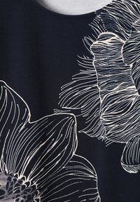 Tissu foncé avec de grands motifs floraux blancs en contour, présentant des pétales détaillés et des éléments centraux d’étamines.